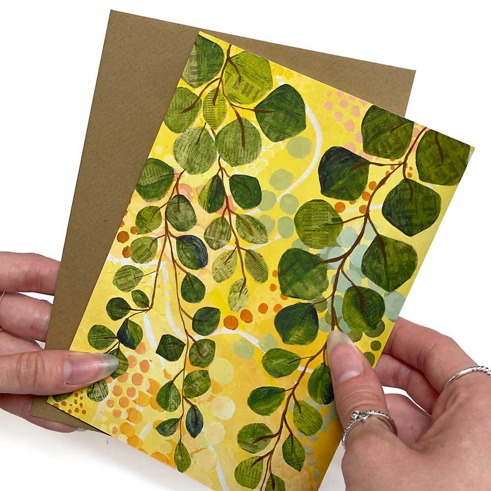 A portrait greeting card of green eucalyptus leaves on yellow, with a kraft envelope